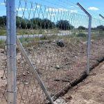 Diamond mesh fencing erected along a long stretch of land next to a road