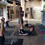 Pilates coach Leonard Lubbe stretching the legs upwards of one of his clients during a class while the clients are lying on their backs