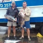 Two fishermen holding their fish in front of Lucky Sands boat in Shelly Beach