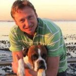 Leonard Lubbe clutching his bulldog while standing inside the surf on the beach at sunrise