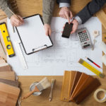 house plan on table with hands around it holding calculatora