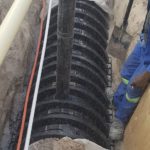 large black sewerage pipeline in open ground with a worker standing next to it