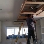 Man on ladder installing underdeck ceiling in kitchen