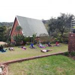 clients lying on mats in the grass outside a building on the south coast KZN doing Pilates with coach Leonard