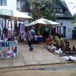 Photograph of people at a flea market outside the Durban Accommodation building, where vendors display their products under huge sun umbrellas.