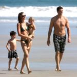 Mother carrying baby walking on the shore with husband and young son in their swimming costumes during the day