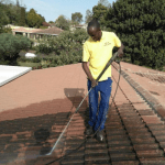 Man on red roof using pressure sprayer to clean off mould