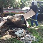 Worker dragging b\large box with rubbish towards flat bed truck in garden