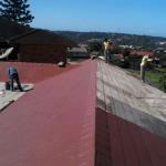 workers on top of a corrogated roof fixing and painting the sheeting