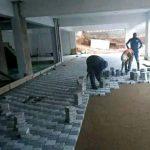 White paving stones and grey pacing stones being laid under a roof on the ground by Indlu Yegagu