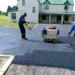 A worker pulling a roller over a road which is being tarred in front of a house