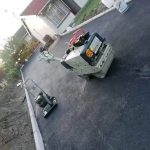 Machinery being used to lay an asphalt tar road alongside houses