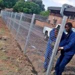 Two workers in blue overhaul;s setting the tension for a wire fence on its extension poles