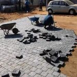 S staff member along with a wheel barrow, laying paving bricks on a gravel surface