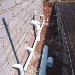 White water pipe line inserted into a brick wall above brown soil