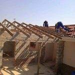 Workers standing on the roof rafters of a brick and cement house they are building