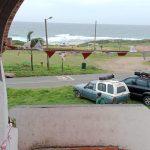 Area outside the Ifafa Beach Hotel shows a parking area with a van in it, as well as a soccer field across the road and the waves of the Ifafa Beach ocean in the background